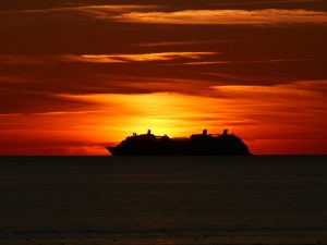 Cruise ship silhouetted against a fiery orange sunset at sea