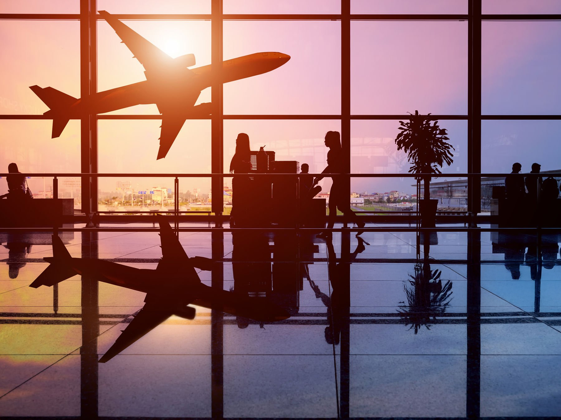 Airplane taking off at sunset with passengers silhouetted inside airport terminal