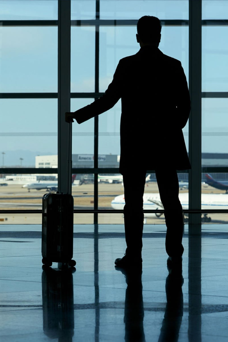 Business traveller with suitcase looking out at airport runway